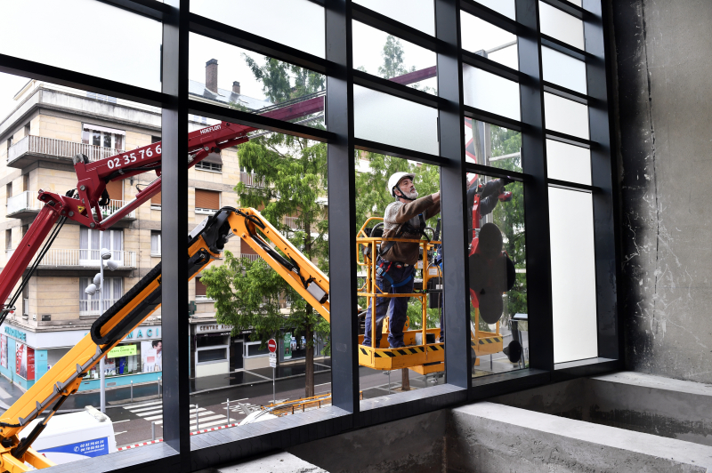 Dans une nacelle, deux salariés positionnent des dalles de verre hissées par la grue.